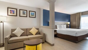 A hotel room with a bed, a sofa, a small table, and framed pictures on the wall. - Comfort Inn & Suites Houston FM1960 - Champions (Houston)