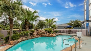 A swimming pool with a stone border, palm trees, and a seating area with umbrellas. - Comfort Inn & Suites Houston FM1960 - Champions (Houston)