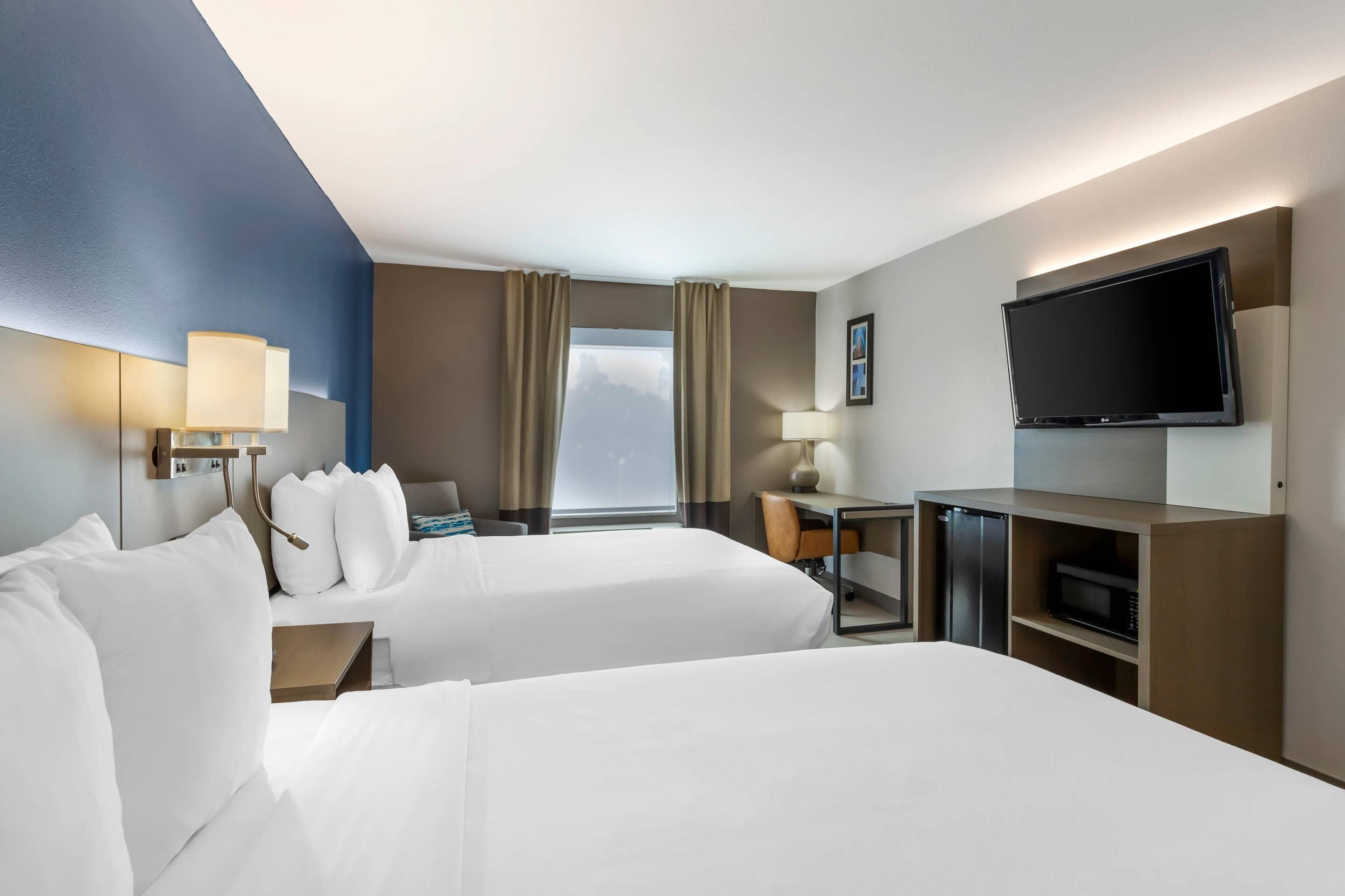 A hotel room with two beds, a desk, a television, and a window with curtains.