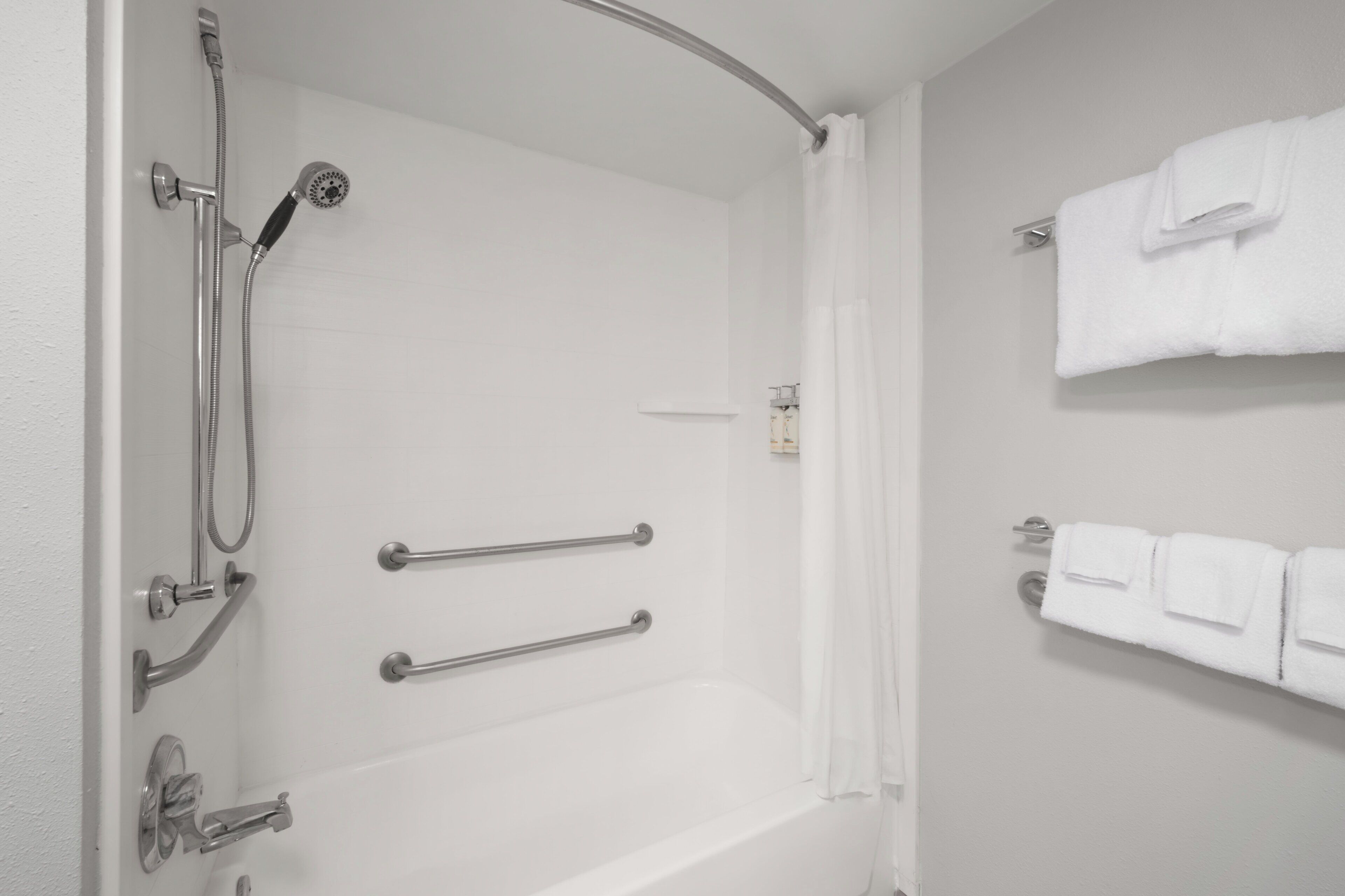 Un baño con bañera, ducha y barras de apoyo. Toallas colgadas en la pared.