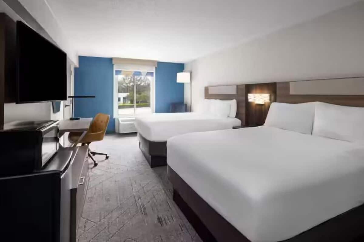 Ein Hotelzimmer mit zwei Betten, einem Schreibtisch mit Stuhl, einem Fernseher und einem Fenster mit Blick ins Freie.