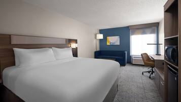 Una habitación de hotel con una cama grande, un escritorio con silla, televisión y ventana con cortinas.