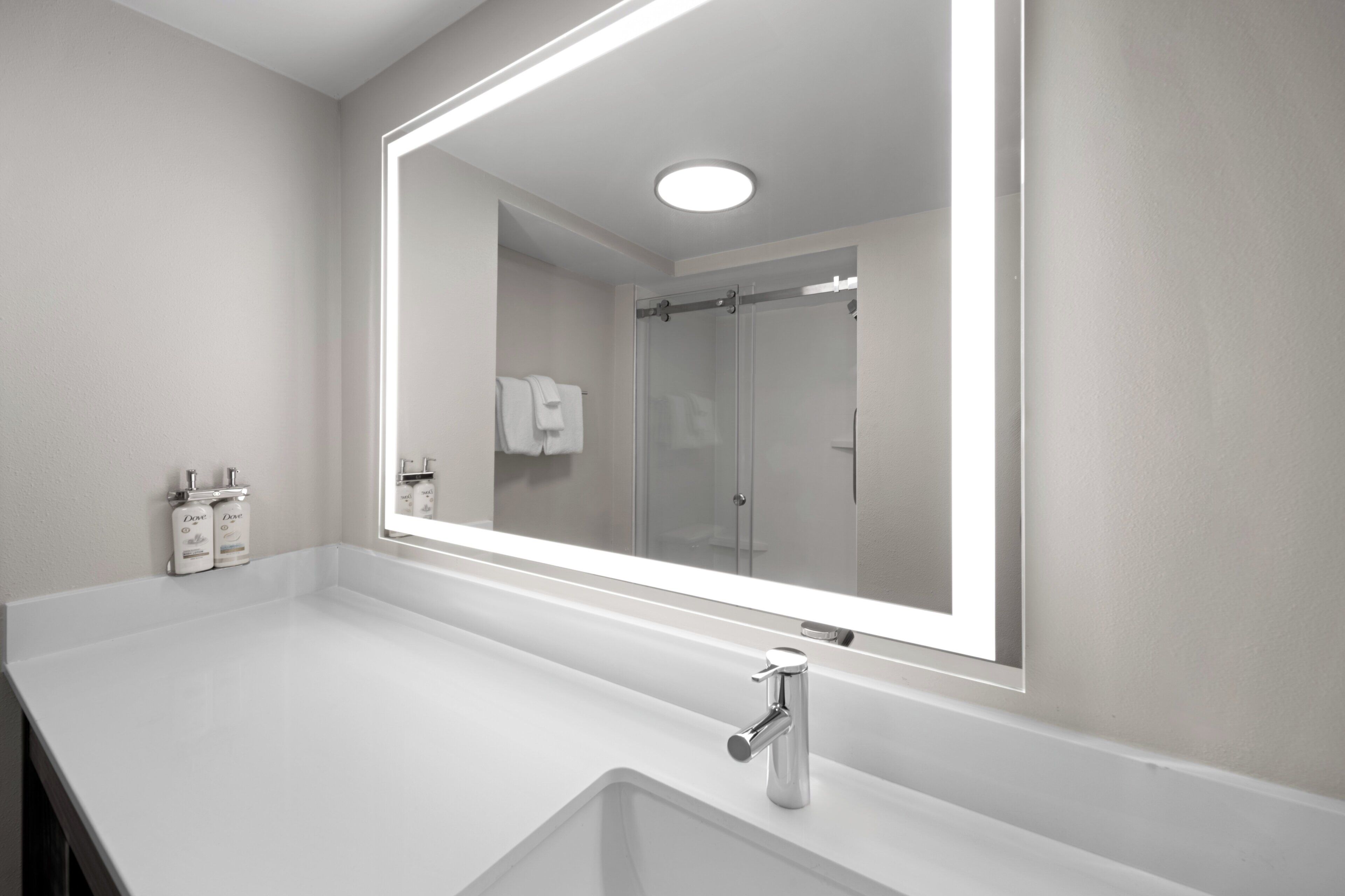 A modern bathroom with a large mirror, white sink, and shower area.
