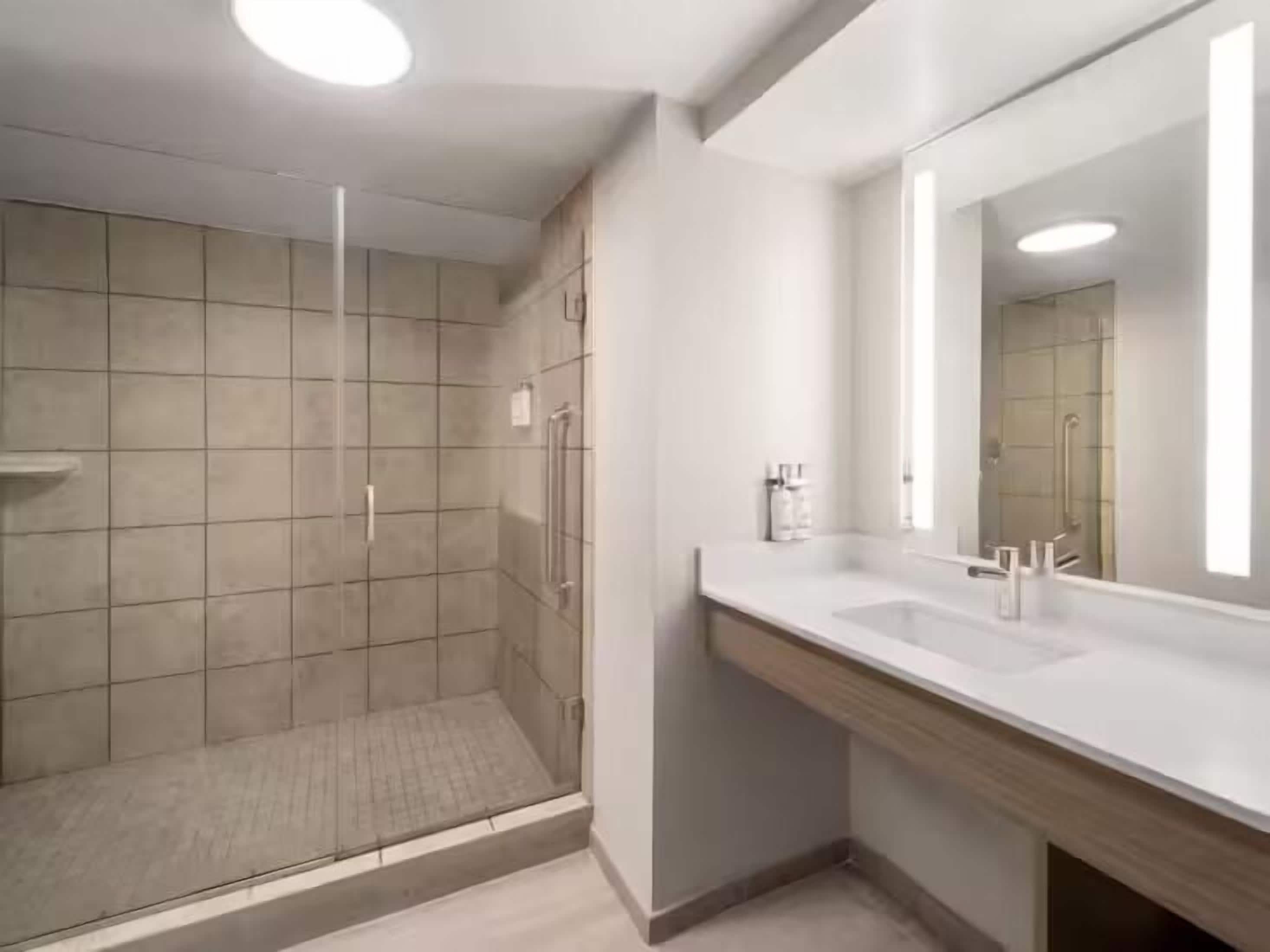 A modern bathroom with a glass-enclosed shower, a large mirror, and a wooden vanity.