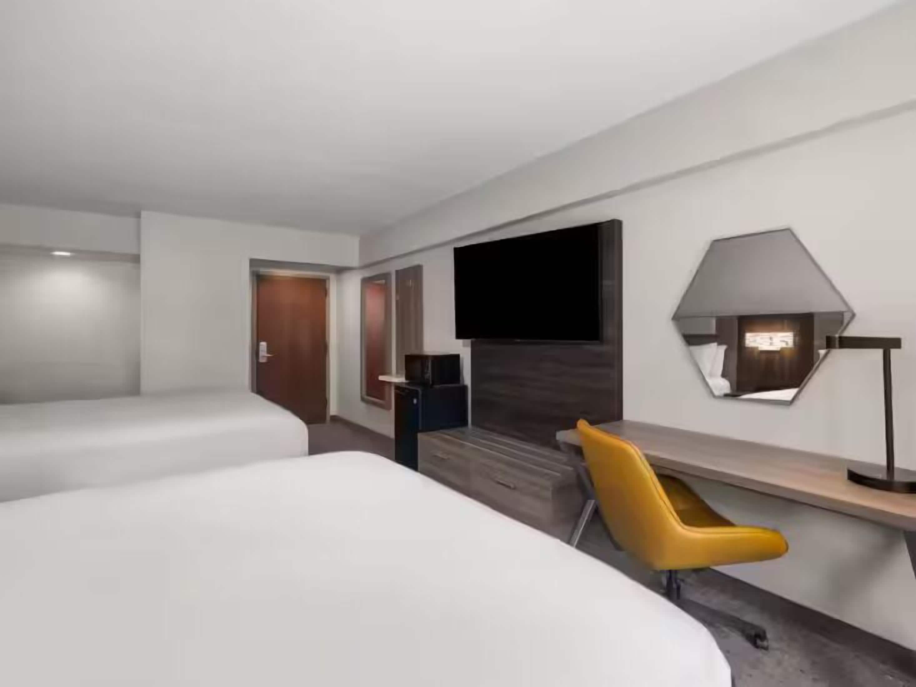 Habitació d'hotel amb dos llits, una taula de treball, una cadira, un televisor i una làmpada.