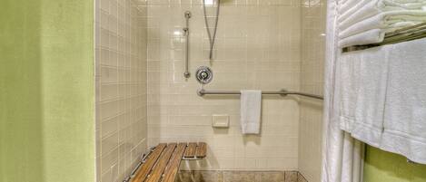A shower area with a wooden bench, a towel rack, and a hand shower.