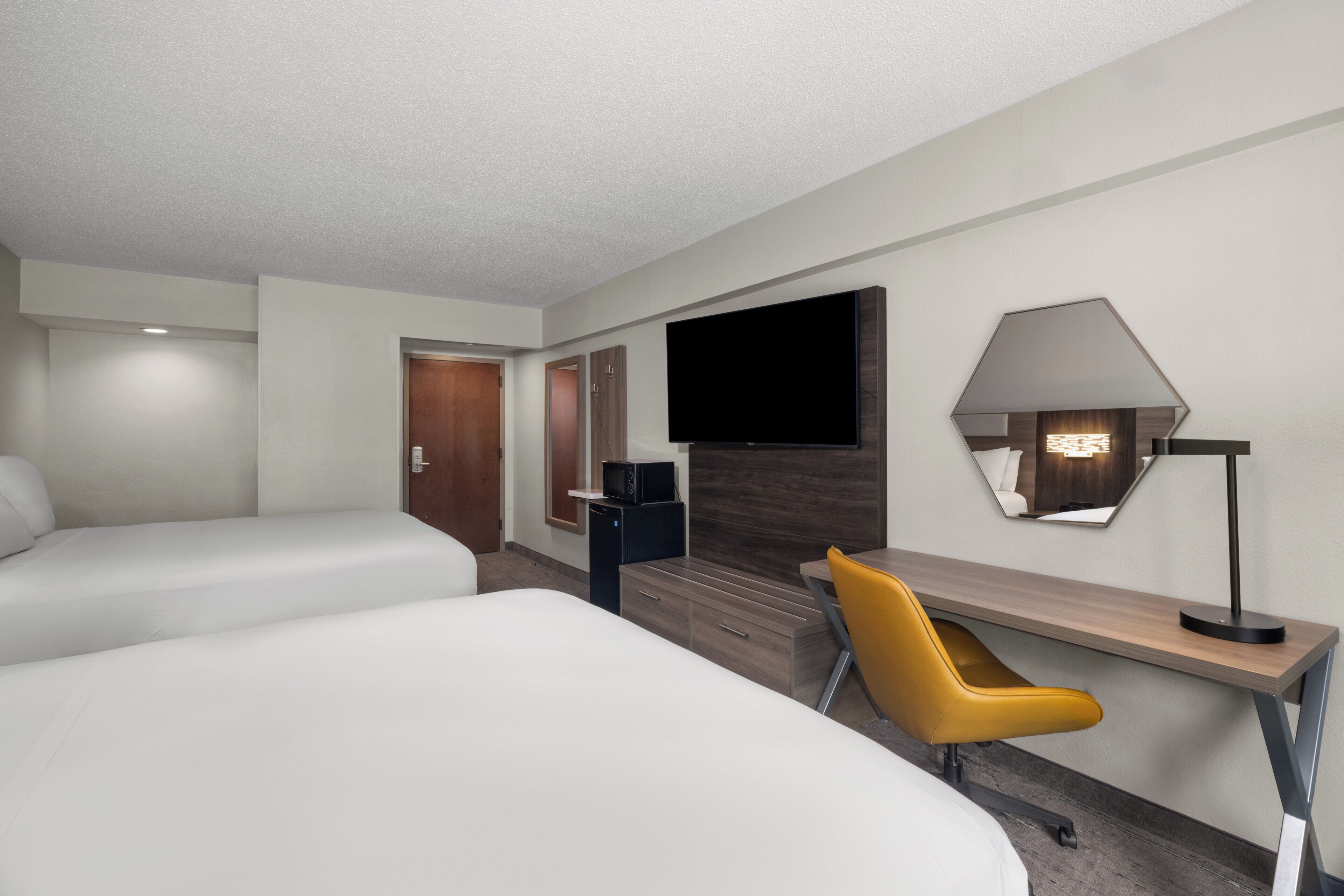 A hotel room with two beds, a desk, a chair, a TV, and a lamp.