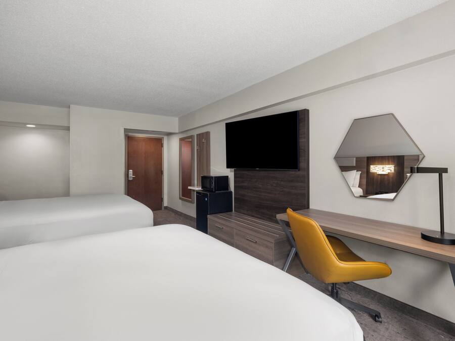 A hotel room with two beds, a desk, a chair, a TV, and a lamp.