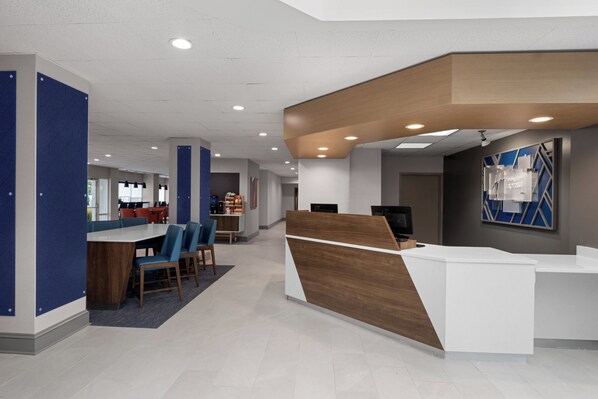 Una moderna zona de recepción con un mostrador de madera, asientos azules y un amplio ventanal que proporciona luz natural.