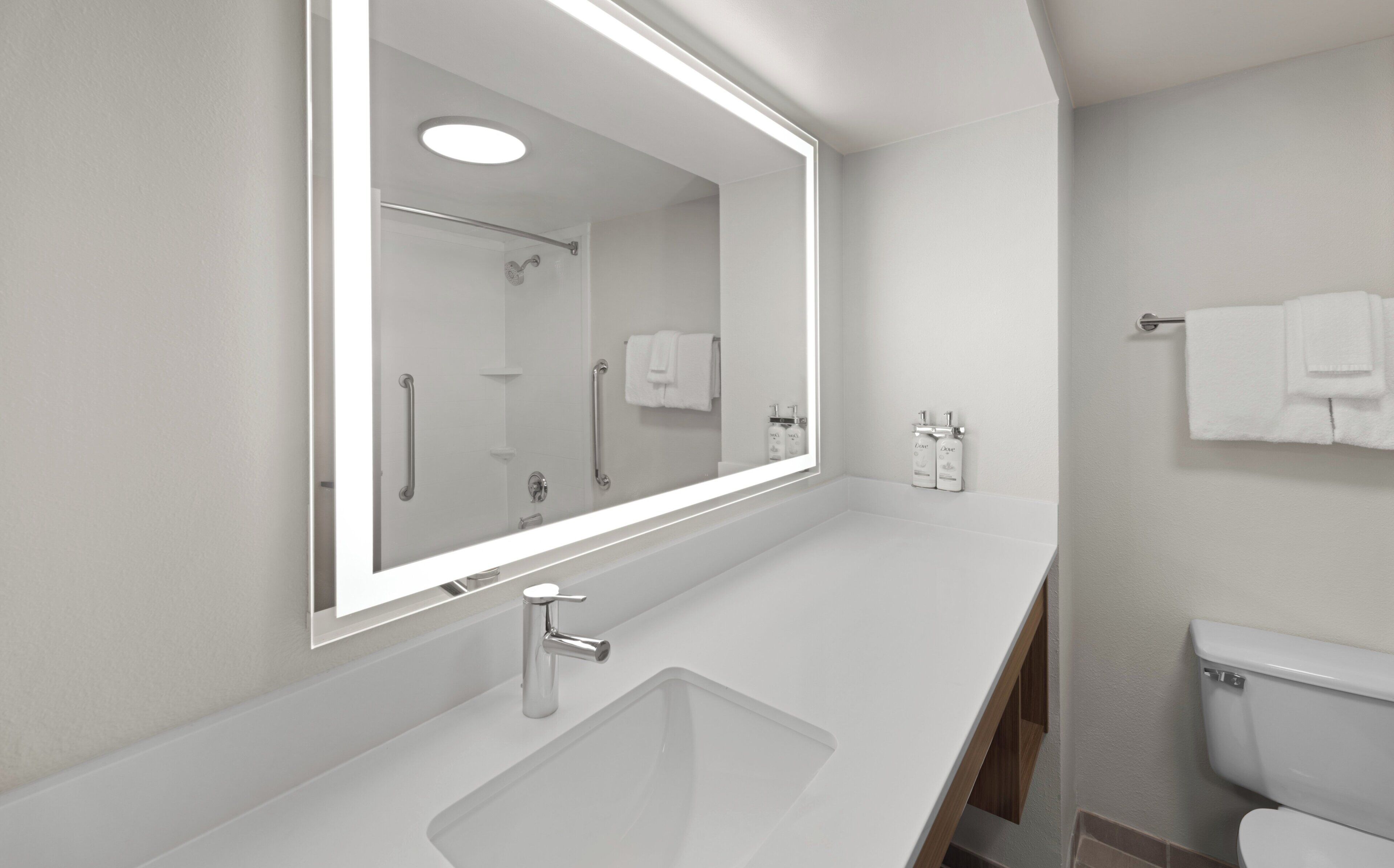A modern bathroom with a large mirror, a sink, a toilet, and a shower.