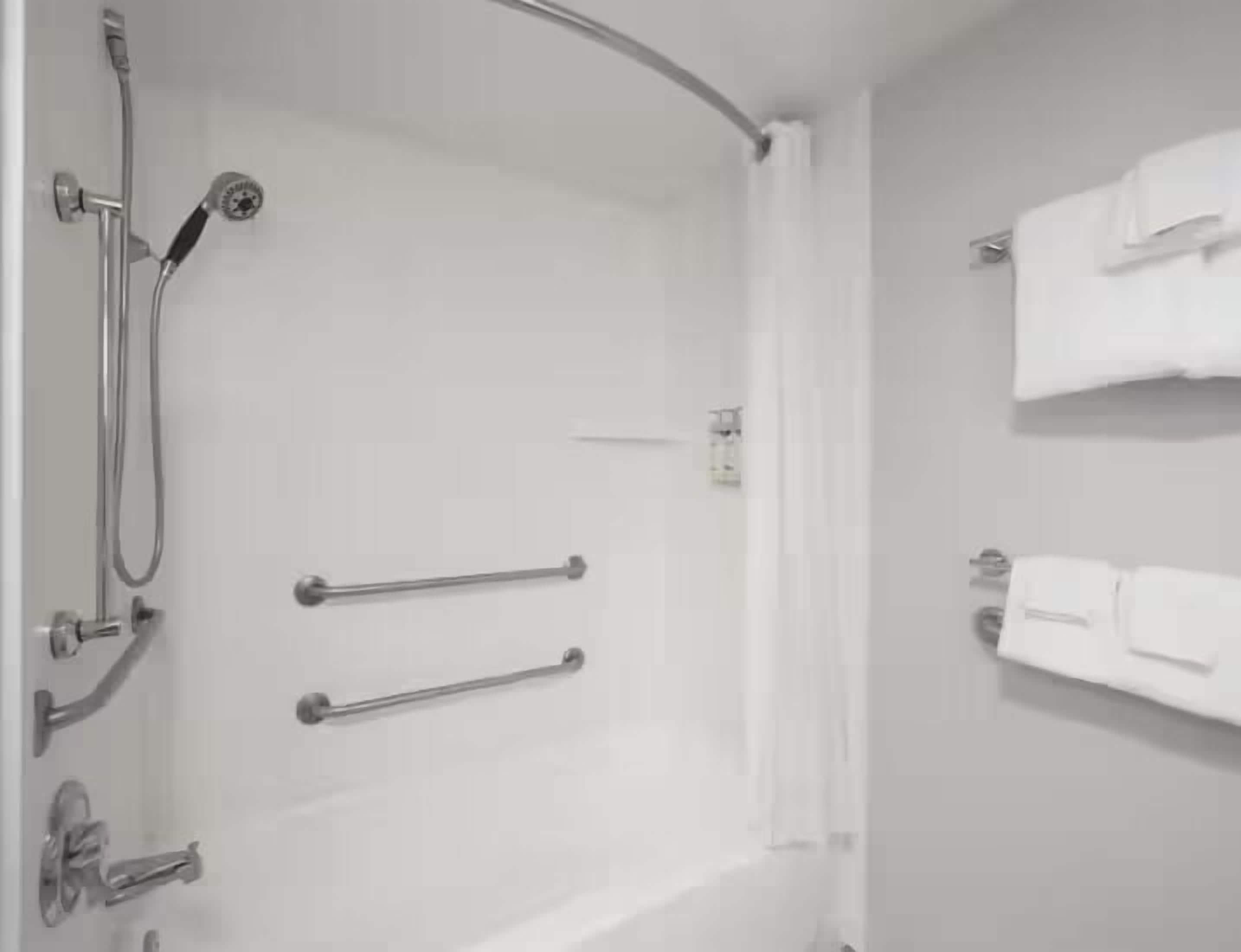 A bathroom with a shower, grab bars, and a towel rack.