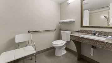 A standard bathroom with a toilet, sink, mirror, and a wheelchair-accessible bench.