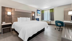 A hotel room with a large bed, bedside tables, a desk with a chair, a window with curtains, and a painting on the wall. - Quality Inn Sandersville (Sandersville)