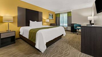 A hotel room with a large bed, a desk, a chair, a TV, and a window with curtains.