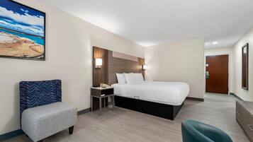 Habitación de hotel con cama, mesita de noche, silla, escritorio y un cuadro en la pared.