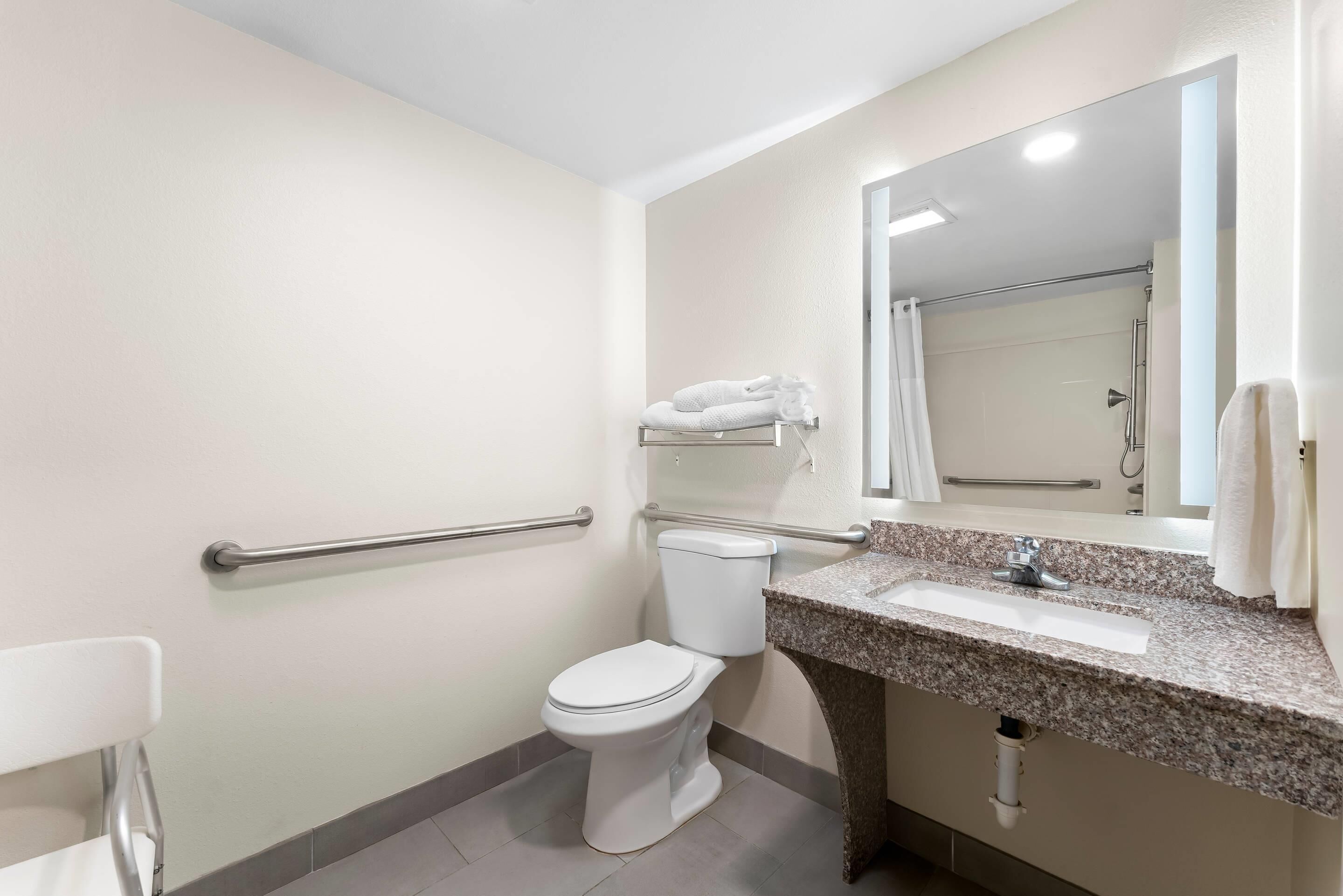 Un baño con inodoro blanco, lavamanos con encimera de granito y espejo sobre el lavamanos.