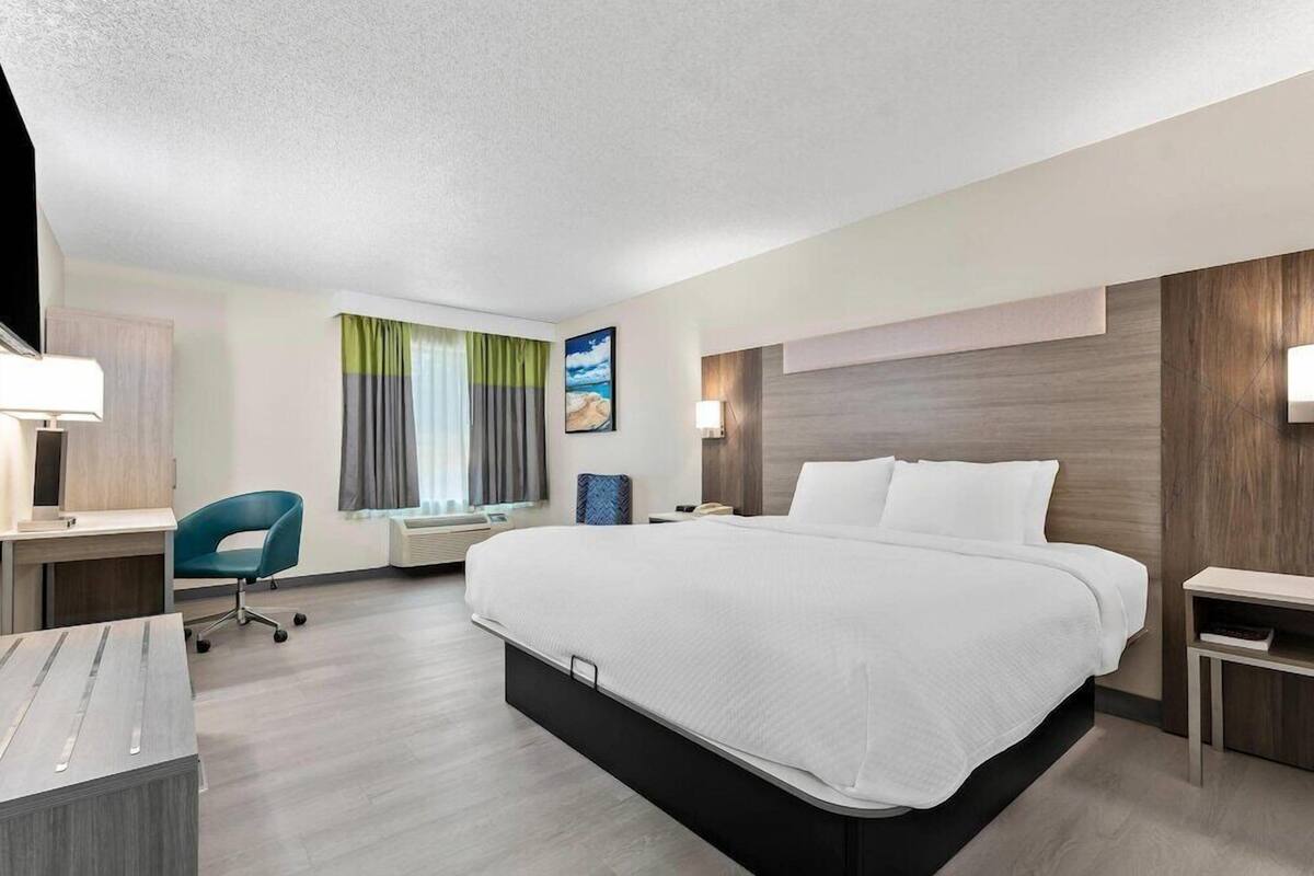 A hotel room with a bed, desk, chair, and a window with curtains.