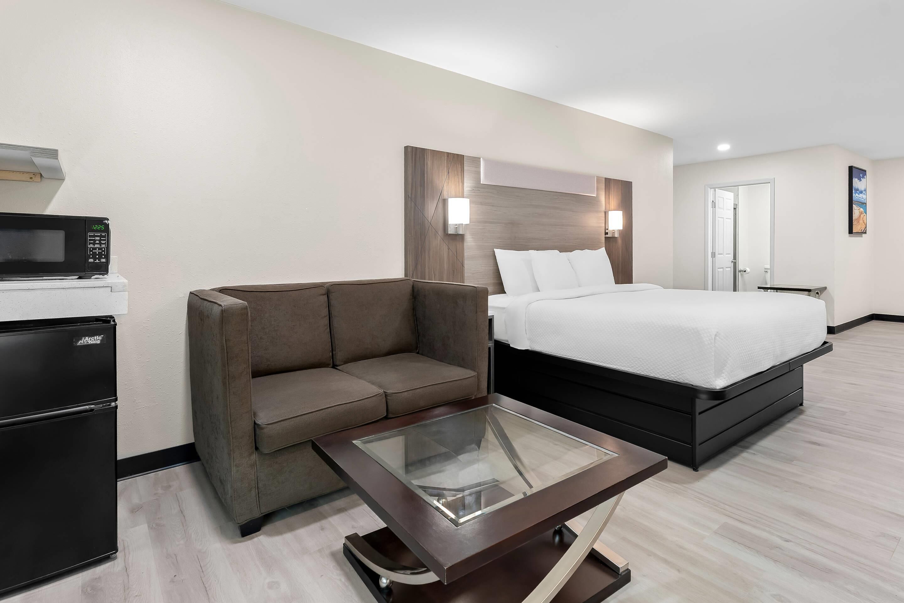 A hotel room with a bed, a sofa, a glass-top coffee table, a microwave, and a refrigerator.