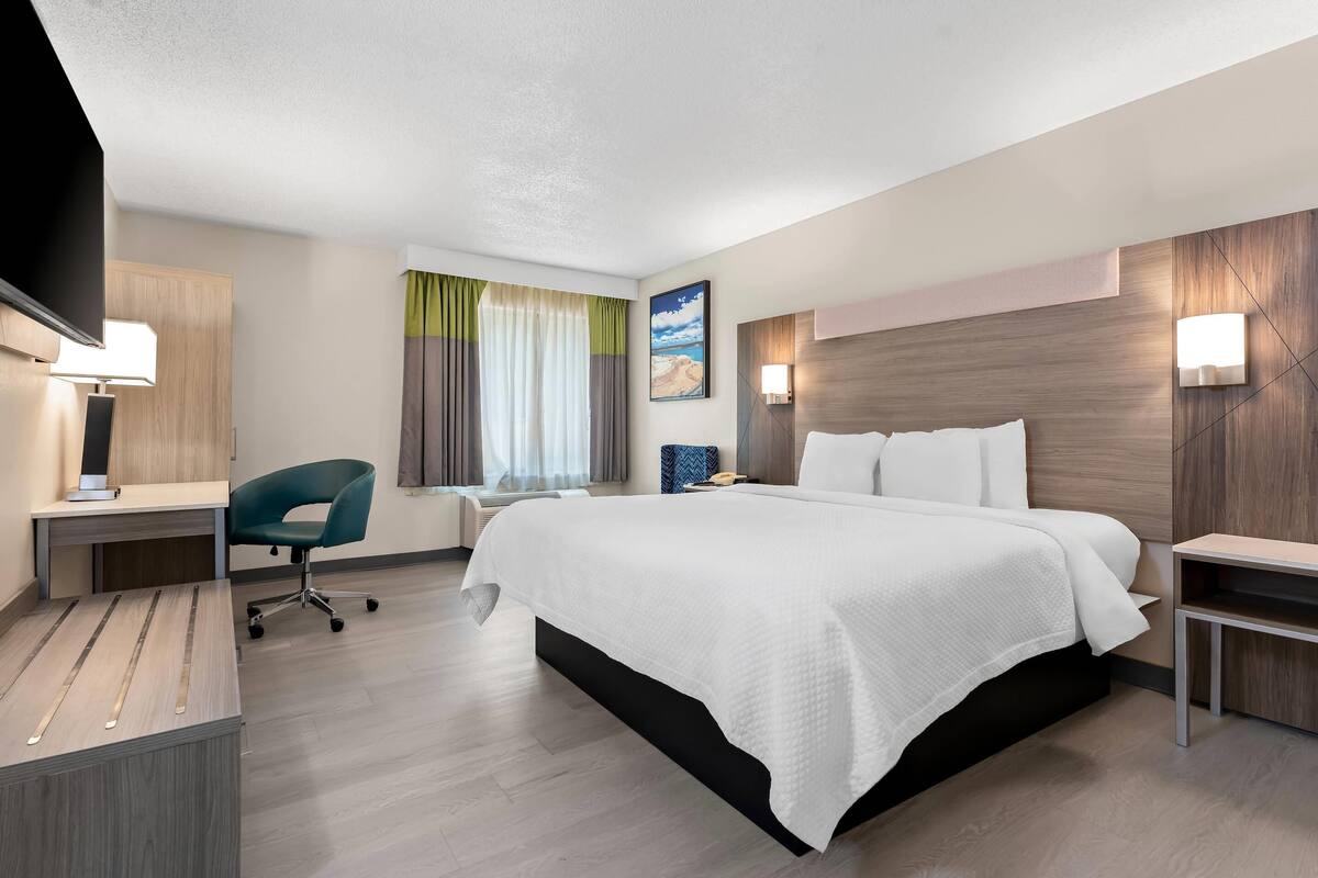 A modern hotel room with a large bed, a desk, a chair, and a TV.