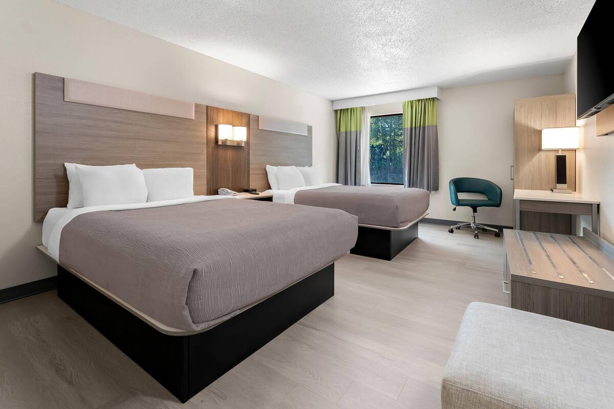 A hotel room with two beds, a desk, a chair, and a TV.