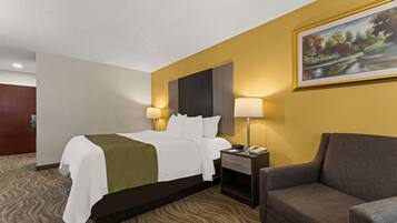 Quarto de hotel com uma cama, duas luminárias de cabeceira, mesa de cabeceira, uma cadeira e um quadro na parede.