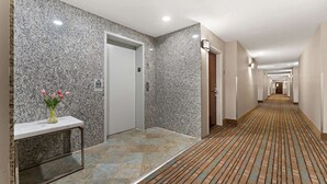 A hotel hallway with a marble wall, a tiled floor, and a carpeted area. - Quality Inn Sandersville (Sandersville)