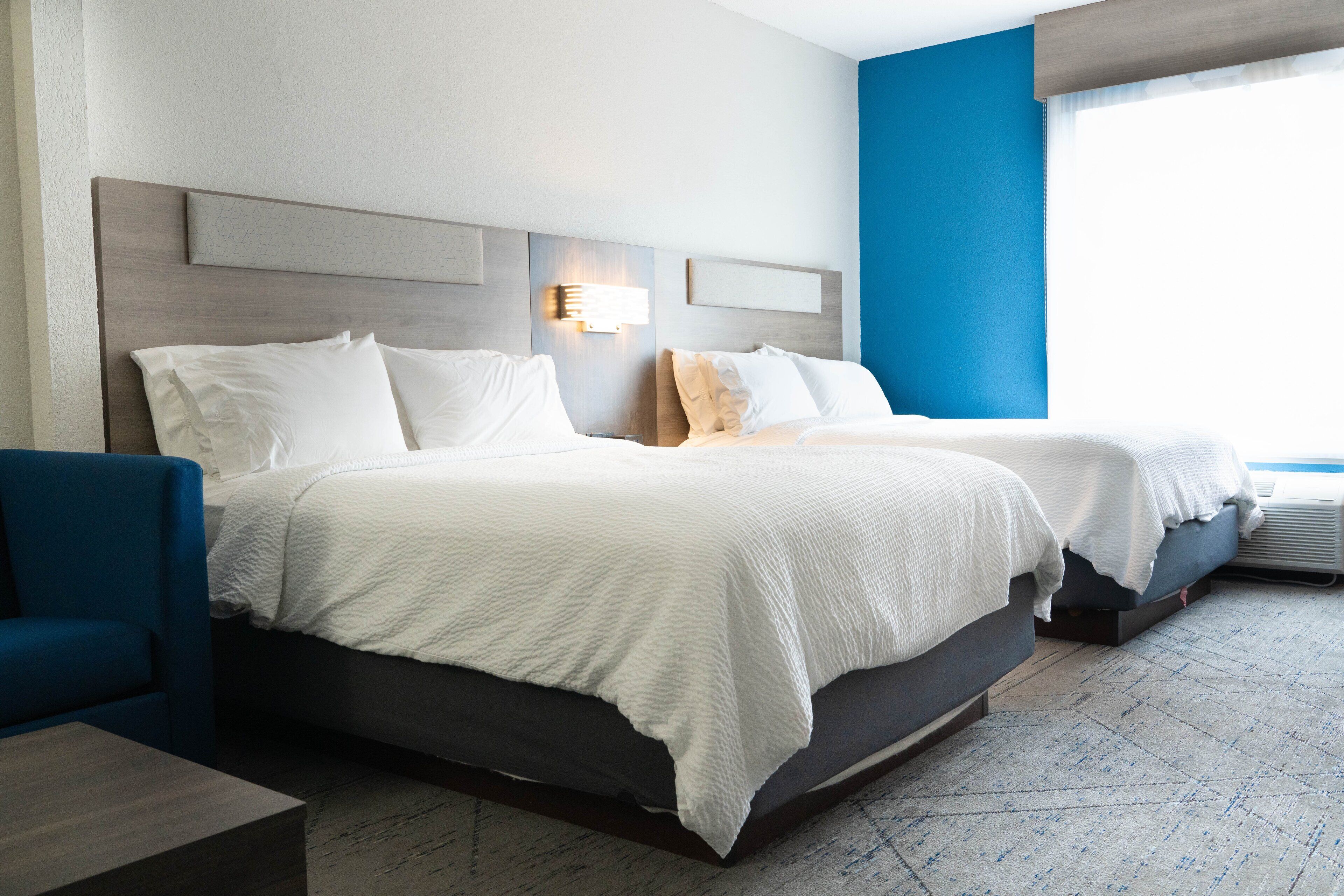 Een moderne hotelkamer met twee bedden, een blauwe fauteuil en een groot raam.