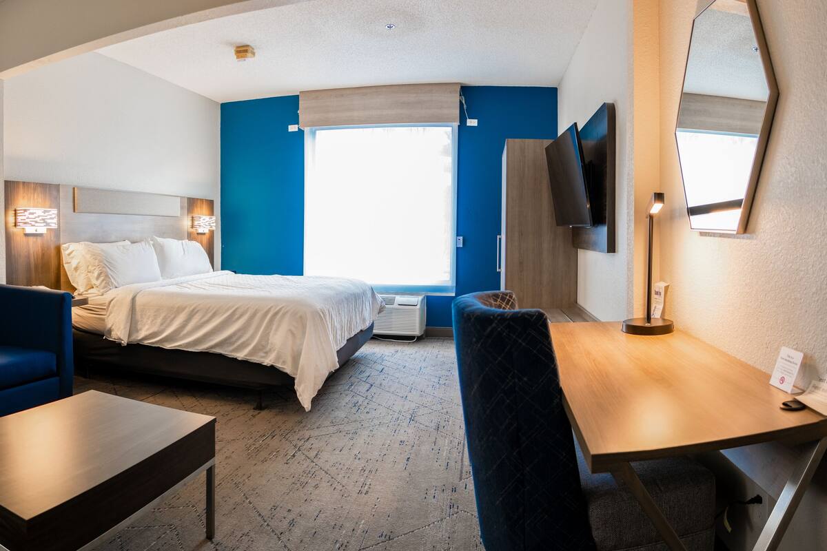 A hotel room with a bed, a blue sofa, a wooden table, and a desk.
