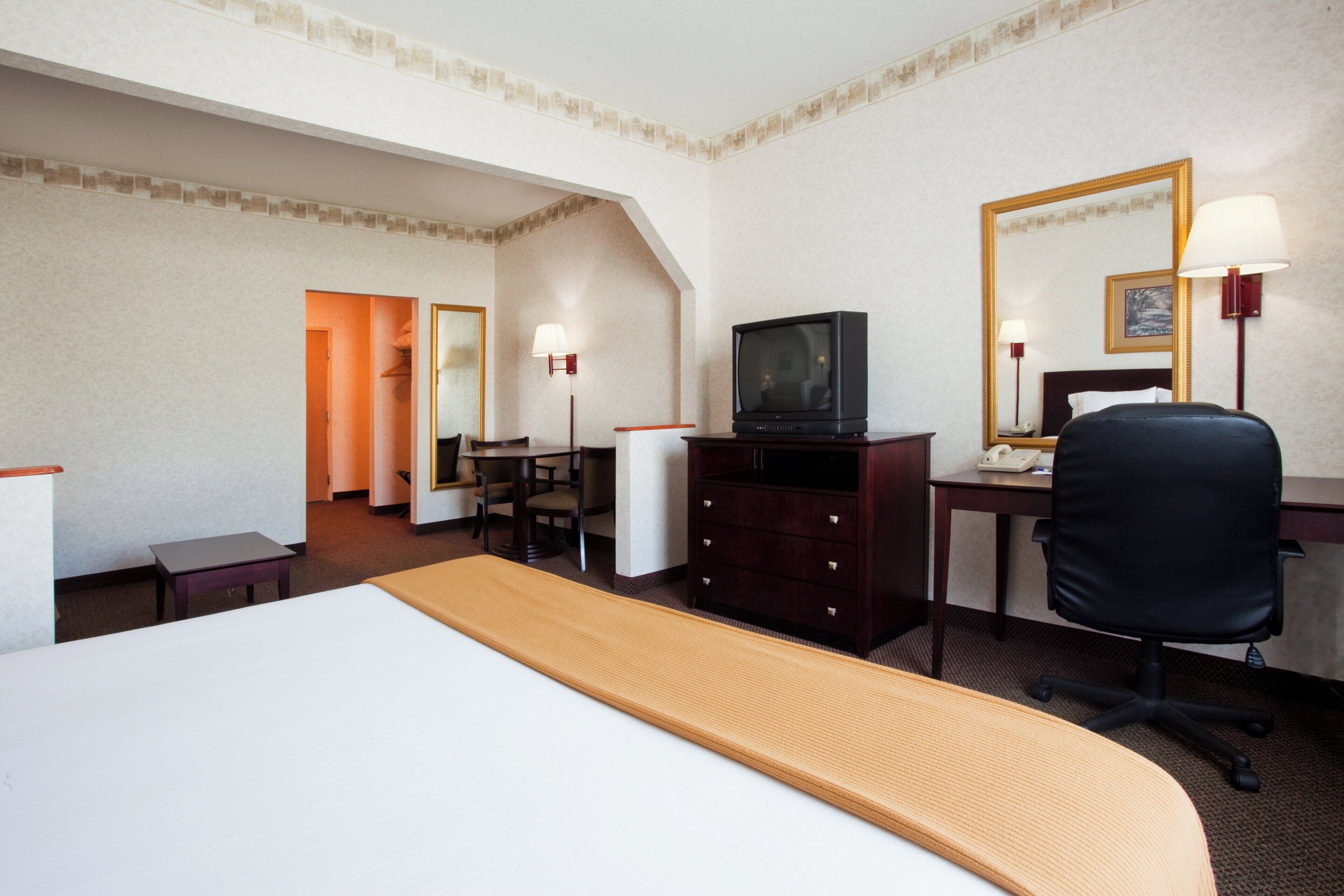 Ein Hotelzimmer mit Bett, Schreibtisch mit Stuhl, Fernseher und Spiegel.