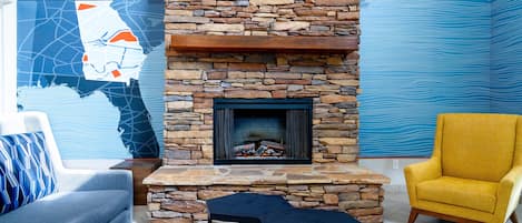 Un salón con chimenea de piedra, un sofá, un sillón amarillo y una obra de arte con un mapa en la pared.