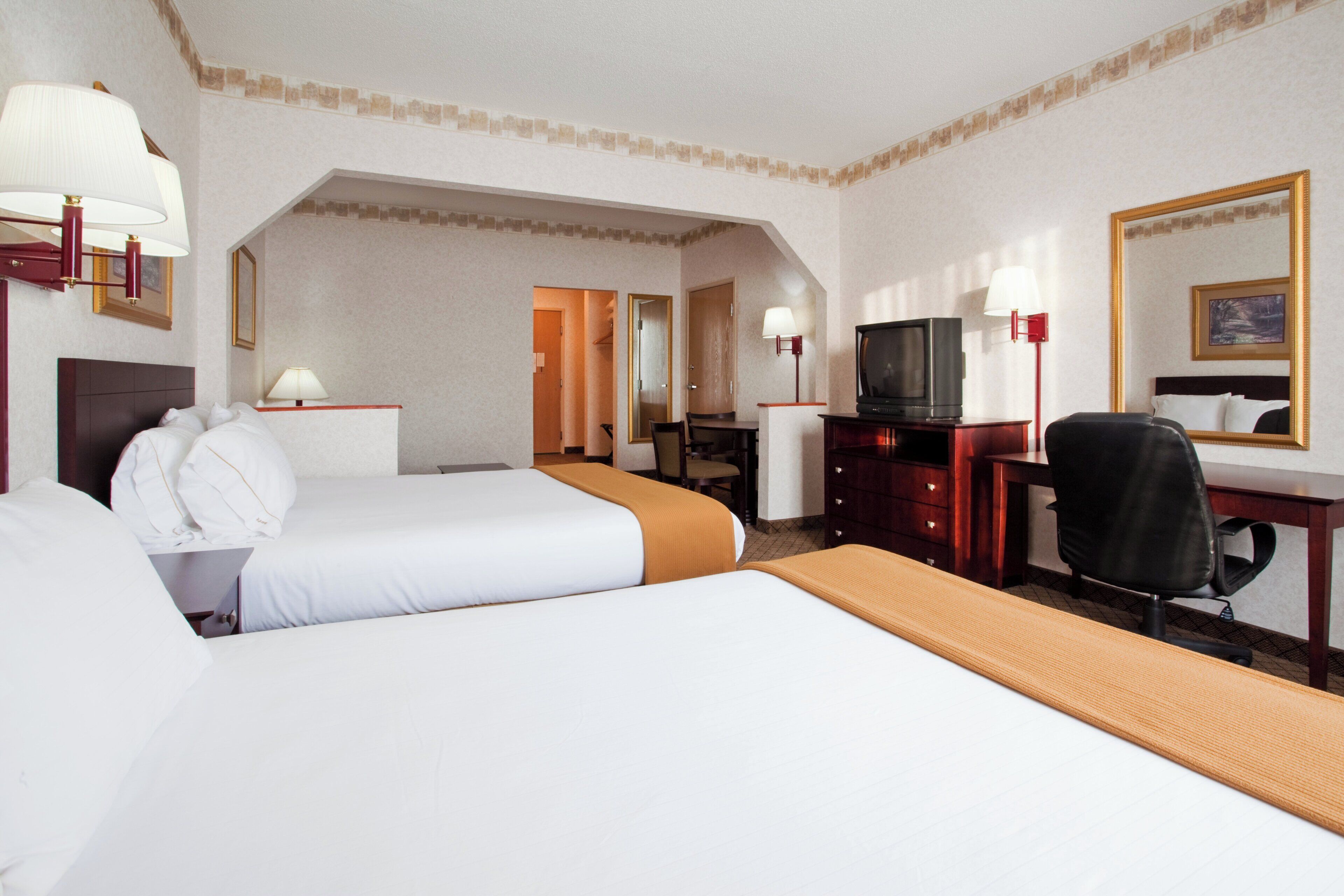 A hotel room with two beds, a desk, a television, and a chair.