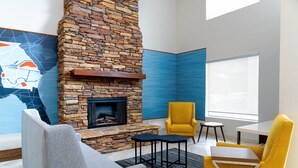 A modern living room with a stone fireplace, a yellow armchair, a grey sofa, and a small table. - Holiday Inn Express & Suites Hiawassee by IHG (Hiawassee)