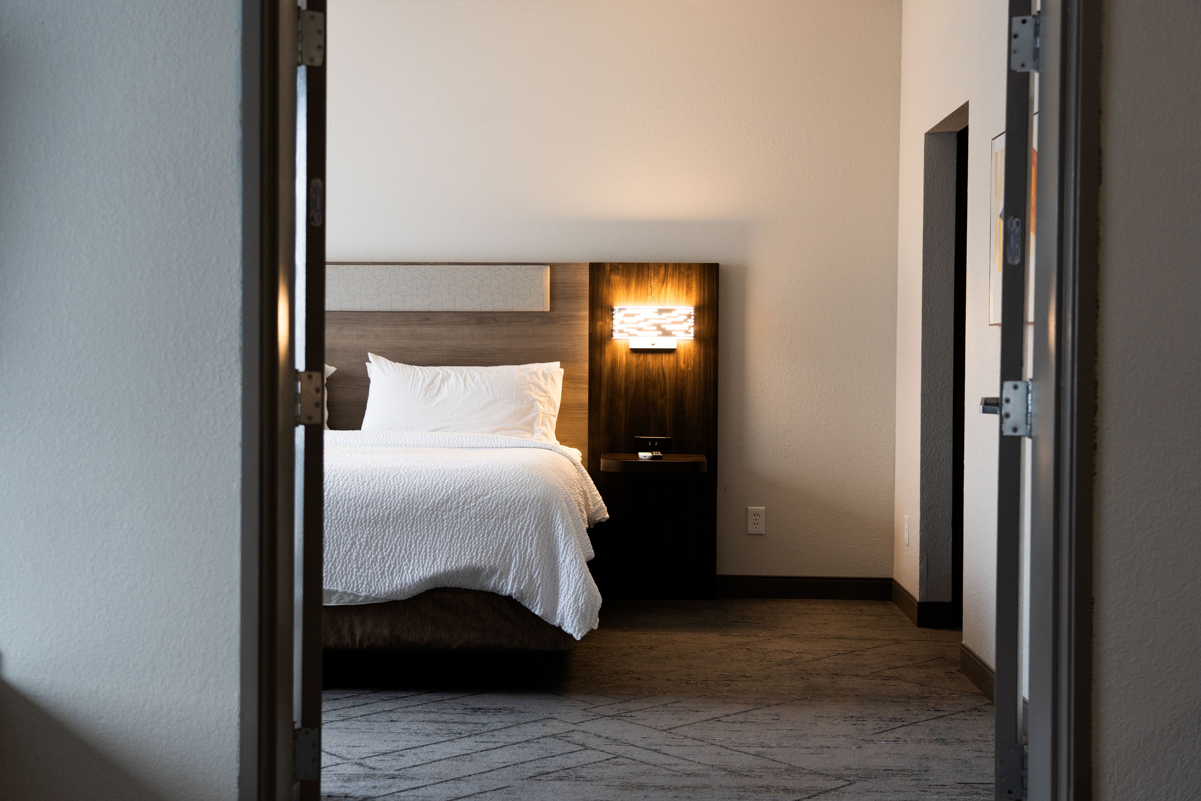 Habitación de hotel con cama, mesita de noche y lámpara de pared.