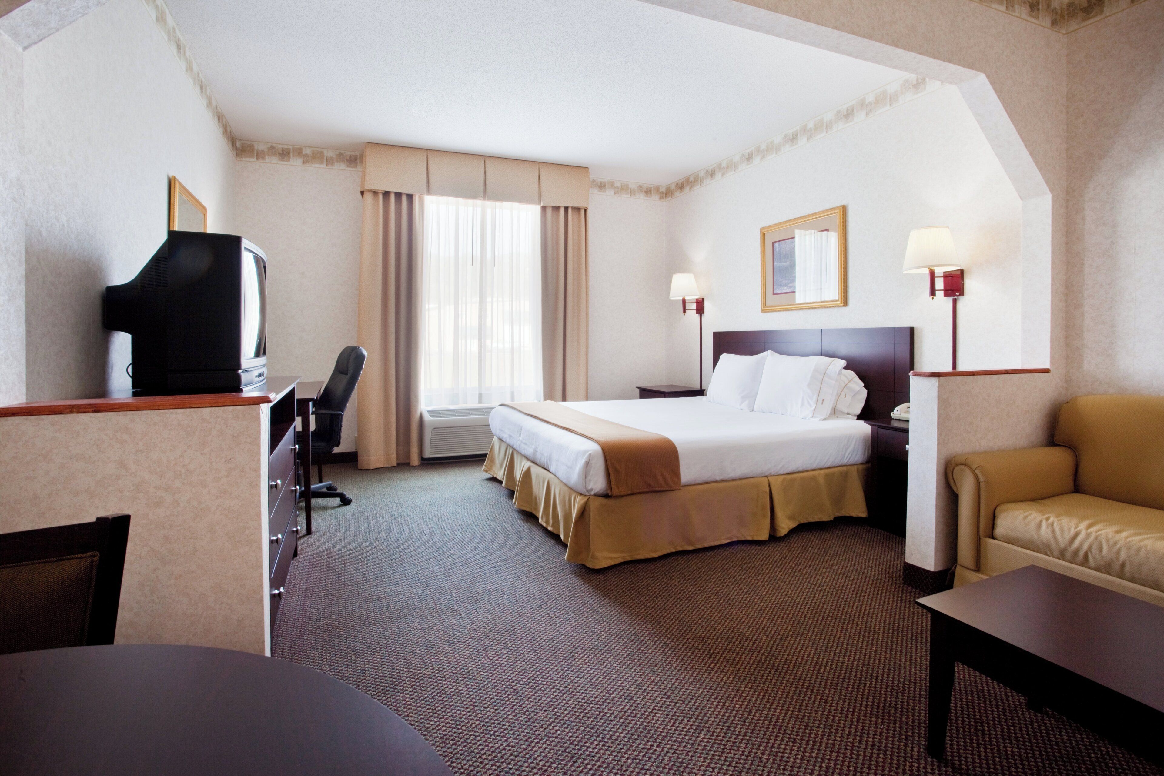 A hotel room with a bed, a desk, a television, a chair, and a sofa.