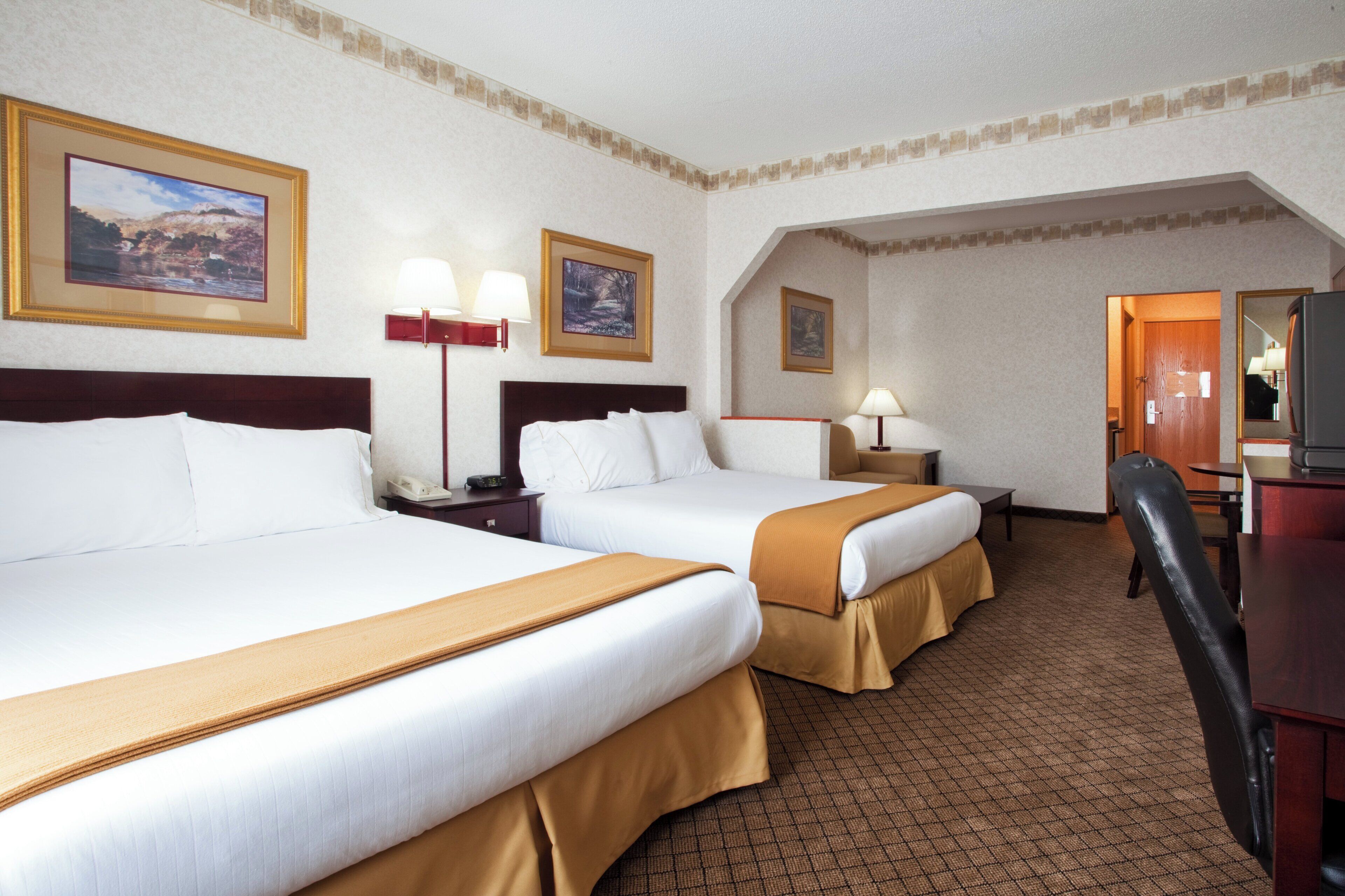 Une chambre d’hôtel avec deux lits, un bureau, une chaise et un téléviseur.