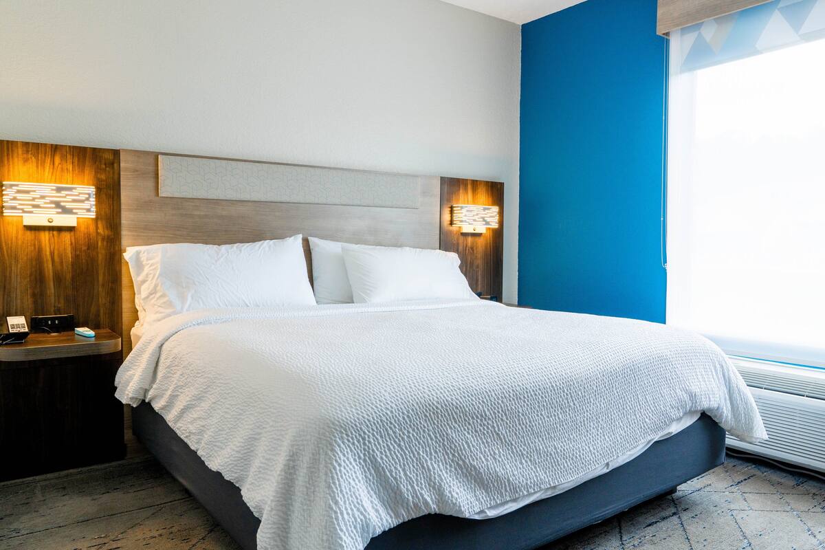 A modern hotel room with a large bed, wooden headboard, and two bedside lamps.
