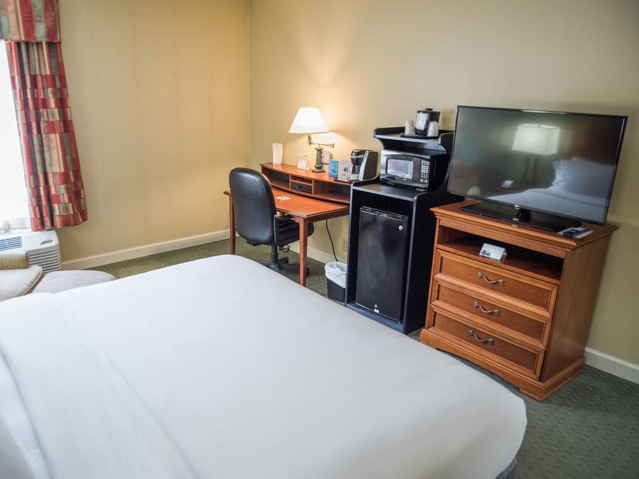 Una habitación de hotel con una cama, un escritorio con una computadora, un televisor y un microondas.