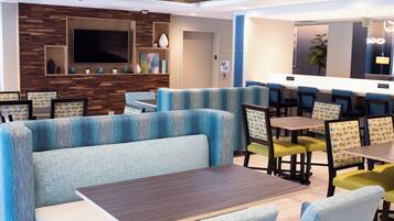 A modern restaurant with booths and tables, a flat-screen TV, and a wooden accent wall.