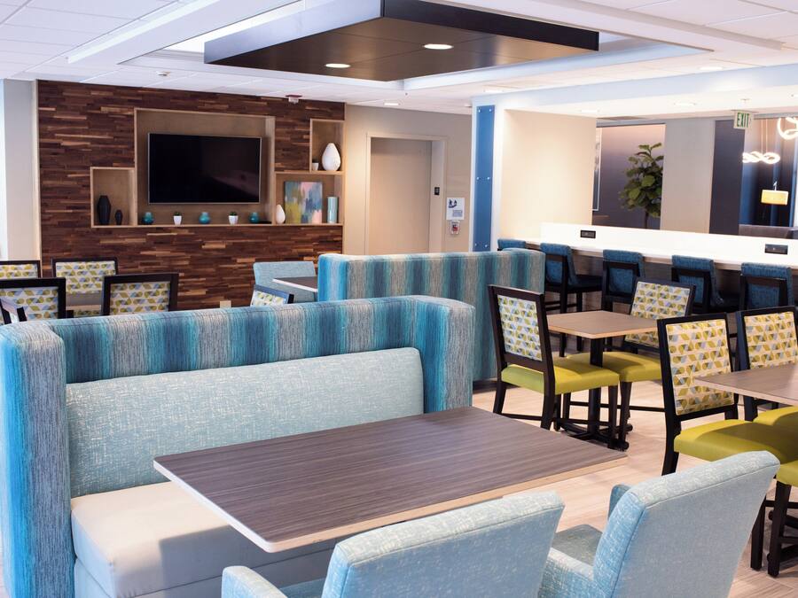 A modern restaurant with booths and tables, a flat-screen TV, and a wooden accent wall.
