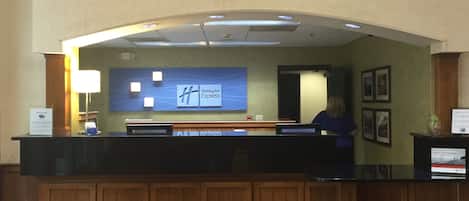 A reception desk with a Holiday Inn Express sign, a lamp, and framed pictures on the wall.