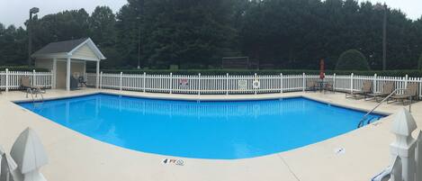 A swimming pool with a white picket fence, lounge chairs, and a small gazebo.