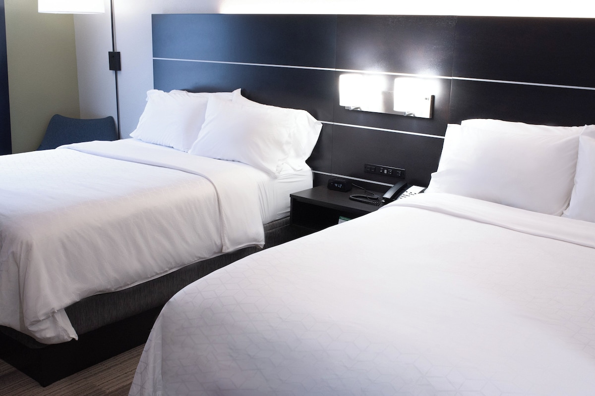 A hotel room with two beds, a nightstand with a phone, and a wall-mounted light fixture.