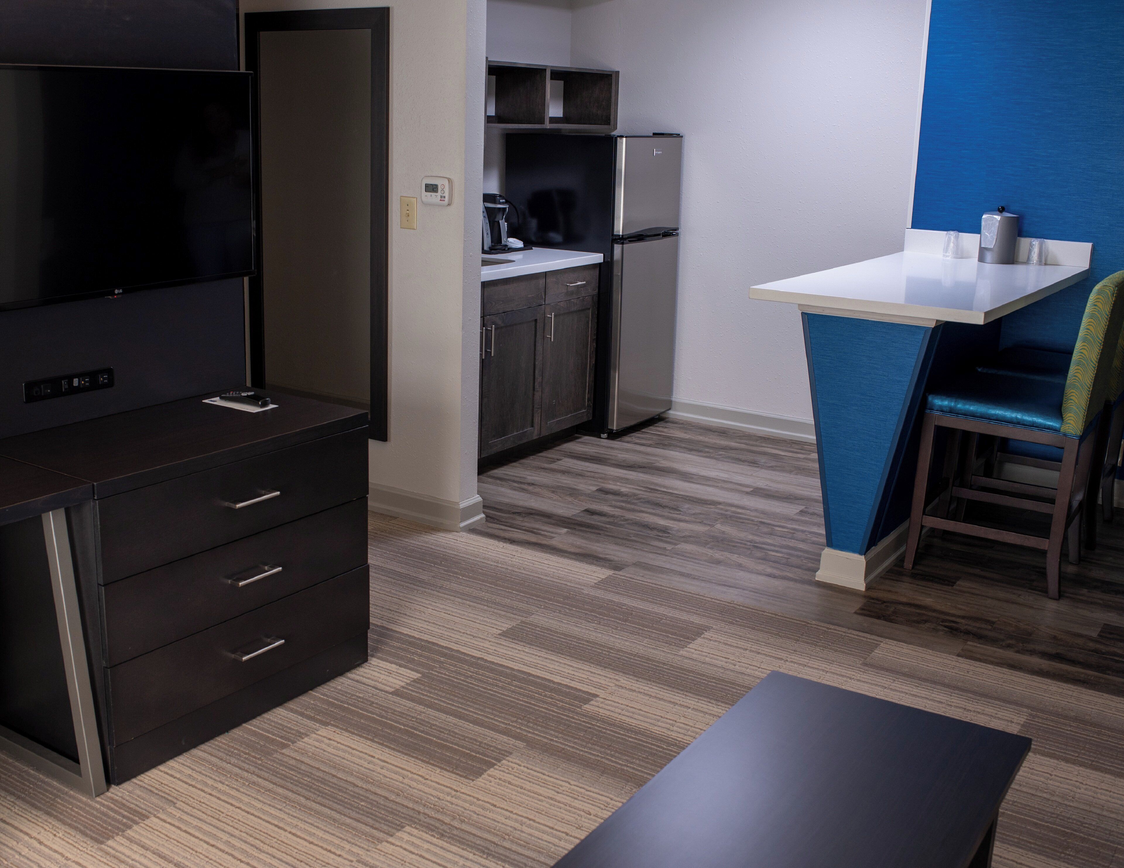 A compact kitchen with a refrigerator, microwave, and coffee maker. There is a small dining area with a table and a chair.