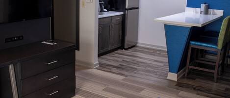 A compact kitchen with a refrigerator, microwave, and coffee maker. There is a small dining area with a table and a chair.