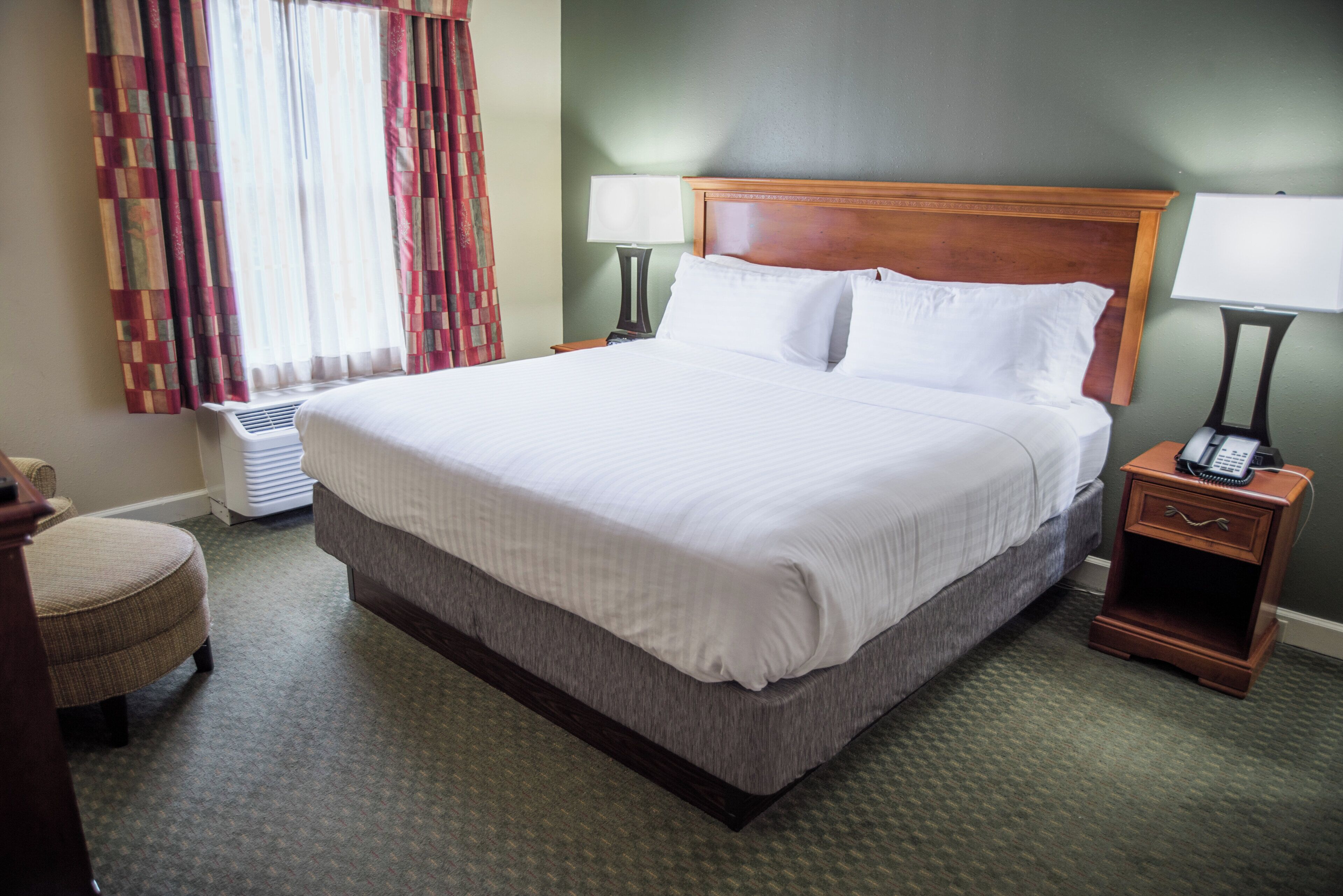 A hotel room with a large bed, a bedside table with a lamp, a chair, and a window with curtains.