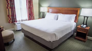 A hotel room with a large bed, a bedside table with a lamp, a chair, and a window with curtains.