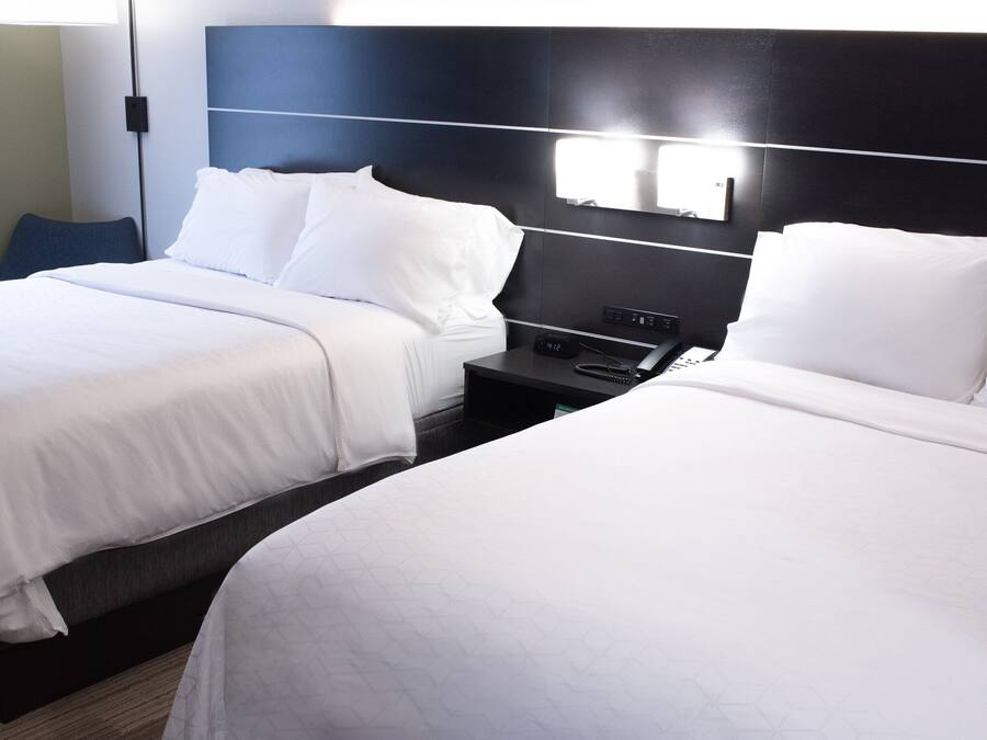A hotel room with two beds, a nightstand, and a wall-mounted light fixture.