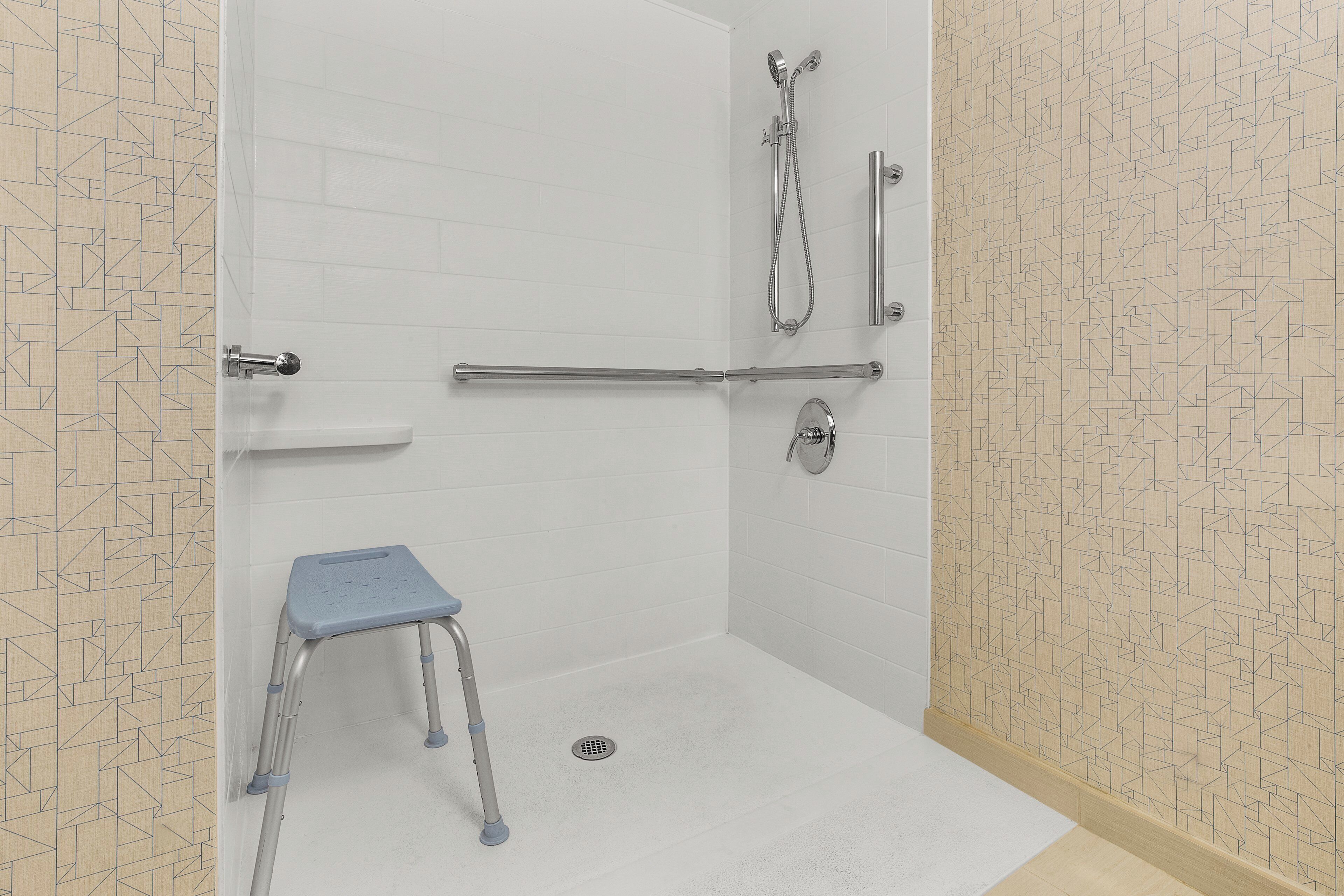 A wheelchair-accessible shower area with a grab bar, a step stool, and a handheld showerhead.