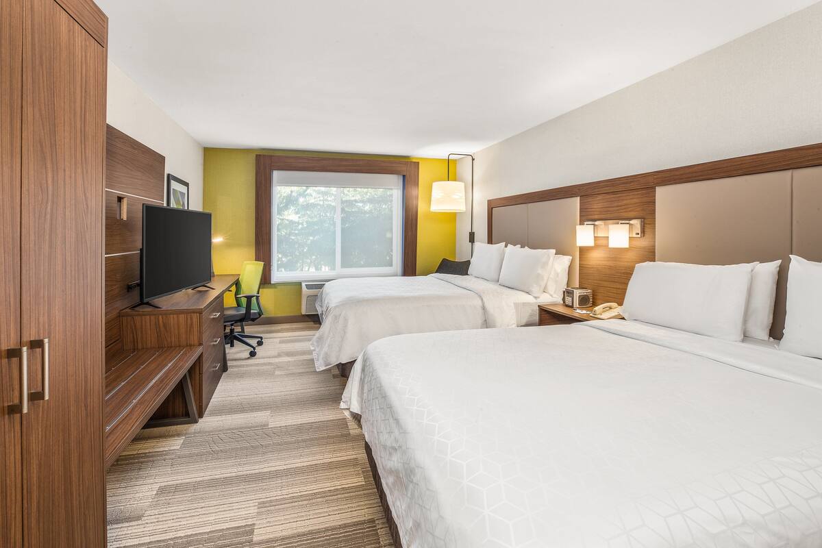 A hotel room with two beds, a TV, a desk, and a window.