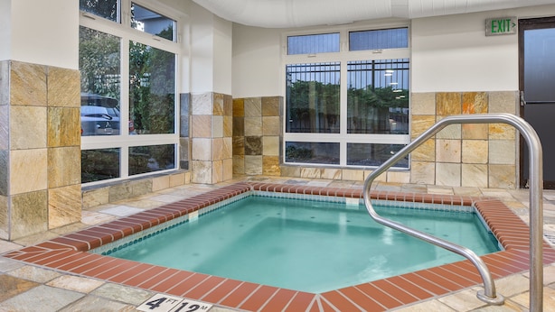 Una piscina interior rectangular con un indicador de profundidad de 1,20 metros, rodeada de baldosas de piedra y grandes ventanales.